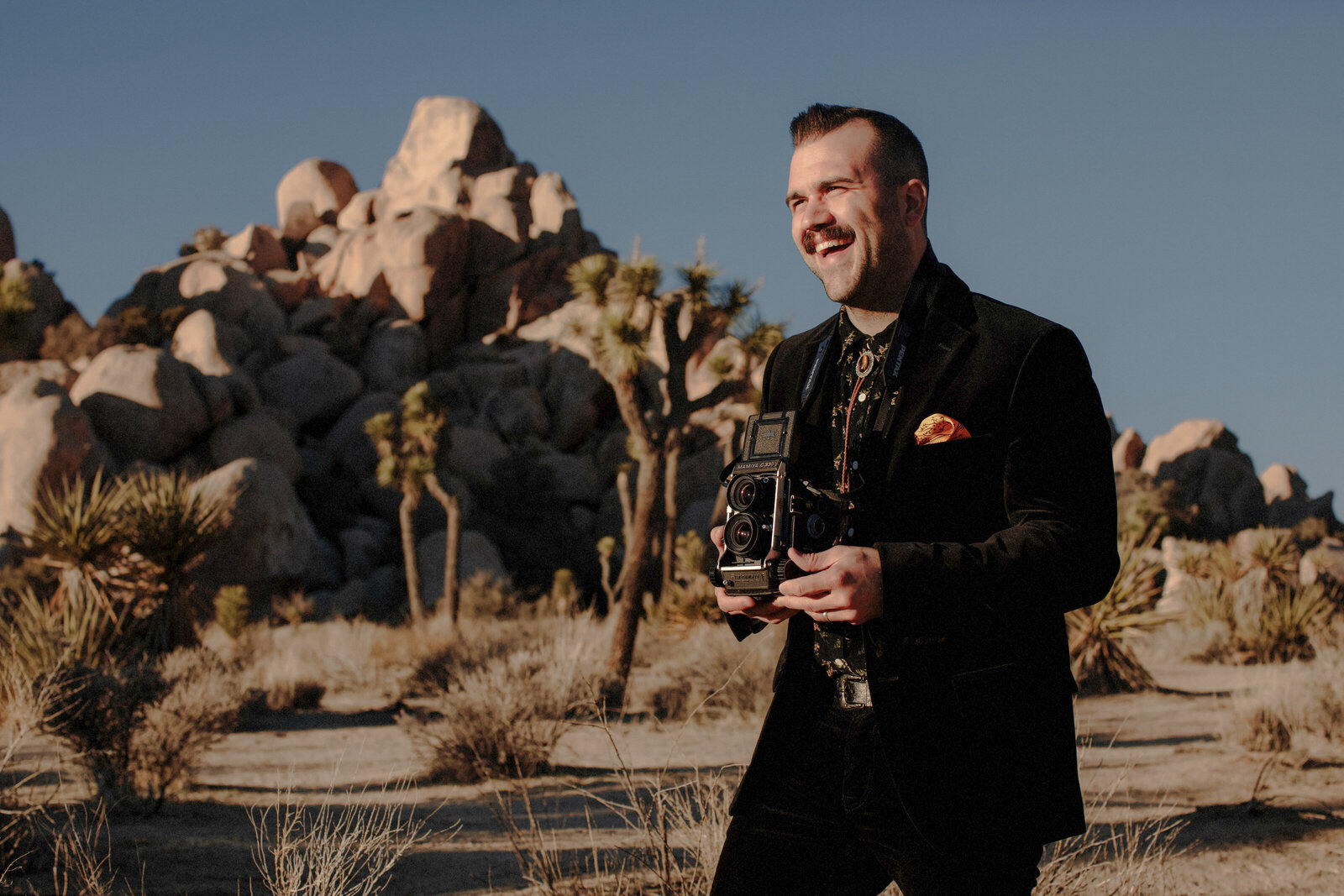 Cody Harris laughing while holding a medium format film camera in the desert
